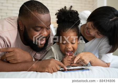 The family has fun and plays education games online with a smartphone at home in the bedroom. Concept of online education and caring from parents. The family has fun and plays education games online with a smartphone at home in the bedroom. Concept of online education and caring from parents. 88434806