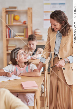 Vertical portrait of young female teacher smiling while helping children during class in school, copy space 88436710
