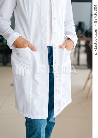 Close-up vertical cropped shot of unrecognizable female doctor in white uniform holding hands in pockets standing in hospital office. Practitioner woman posing at workplace. Concept of medical work. Close-up vertical cropped shot of unrecognizable female doctor in white uniform holding hands in pockets standing in hospital office. Practitioner woman posing at workplace. Concept of medical work. 88436804