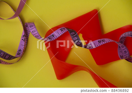 Top view of elastic bend and measuring tape on yellow background 88436892