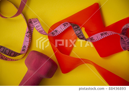 Top view of dumbbell, elastic bend and measuring tape on yellow background Top view of dumbbell, elastic bend and measuring tape on yellow background 88436893