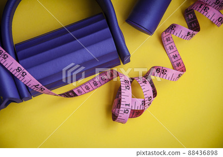 Top view of tummy trimmer and measuring tape on yellow background. Fitness and weight loss concept Top view of tummy trimmer and measuring tape on yellow background. Fitness and weight loss concept 88436898