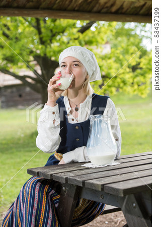 Latvian woman in traditional clothing with milk glass on nature 88437199
