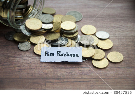 Hire purchase text on torn paper with jar, coins, and wooden table background. Conceptual 88437856