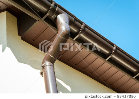 Brown pvc gutter connected to downpipe on roof edge. 88437880