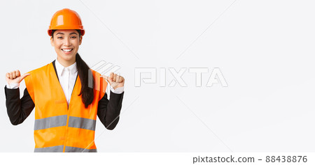 Successful proud smiling asian female construction manager, engineer in safety helmet pointing at herself, show-off. Architect recommend personal assistance, bragging accomplishments 88438876