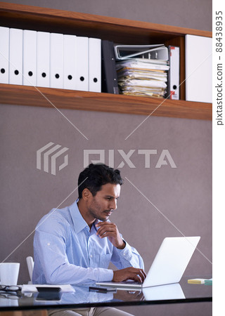 Hes working hard to complete his tasks. Cropped shot of a handsome young businessman working at his desk. 88438935