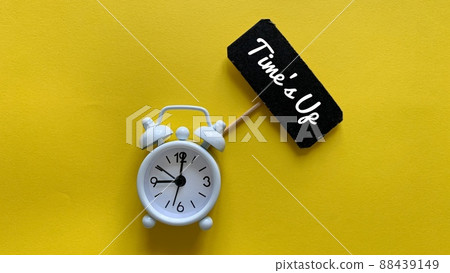 Alarm clock on yellow background with text on small black signage - Time is up. 88439149