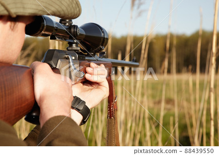 Patience is the secret to a perfect shot. A game hunter looking through the reeds with his sniper rifle. 88439550