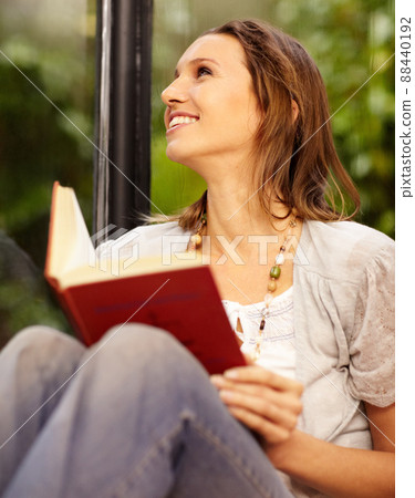 Theres nothing better than relaxing with a good book. A beautiful woman reading while sitting next to a window. 88440192