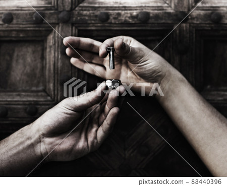 A helping hand. Closeup of two hands holding a nut and bolt against a wooden door. A helping hand. Closeup of two hands holding a nut and bolt against a wooden door. 88440396