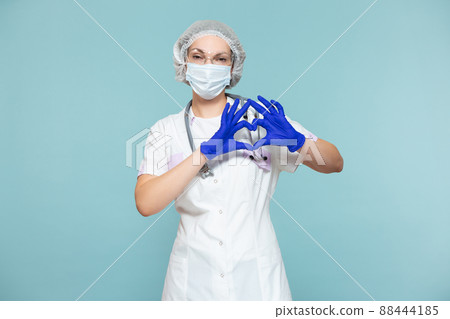 Heart symbol, love. Doctor or nurse woman in a personal protective suit with a stethoscope, on a blue background. In a mask, gloves, goggles and a hat. Copy paste. healthcare concept. Heart symbol, love. Doctor or nurse woman in a personal protective suit with a stethoscope, on a blue background. In a mask, gloves, goggles and a hat. Copy paste. healthcare concept. 88444185