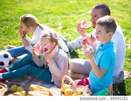 Happy parents with children on picnic eating watermelon in summer park Happy parents with children on picnic eating watermelon in summer park 88445181