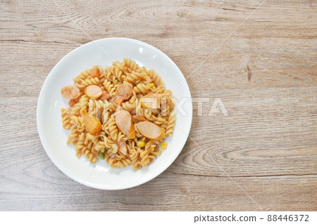 stir fried Gemelli Italian pasta with slice pork sausage and garden pea with corn in ketchup on plate 88446372