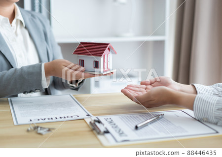 Insurance concept the estate agent holding a house model and giving it to his client 88446435