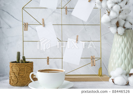 White home office room interior, bloggers workplace. Cup of coffee. Mood board with postcards and reminders mockup. Cotton branches in a vase, interior decoration. Freelance workplace 88446526