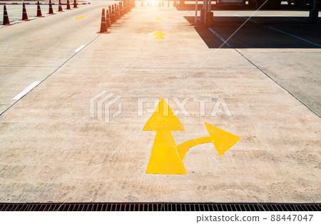 The yellow arrow on the concrete road marks the entrance to the parking lot. Arrow on the road, yellow colour photo. Arrow on the road in an outdoor parking lot. photo of yellow arrows on the road. 88447047