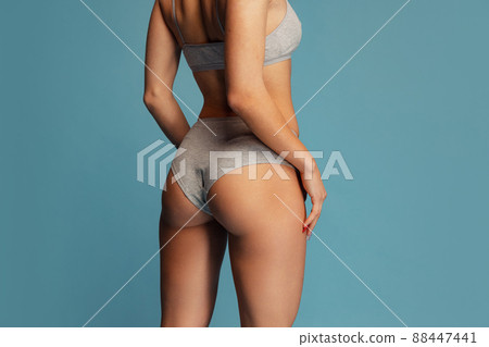 Side view studio shot of cropped female body in gray underwear posing isolated over blue background. 88447441