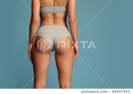 Studio shot of slim, sportive female body in gray comfortable underwear isolated over blue background. Sportive bottocks, legs 88447443