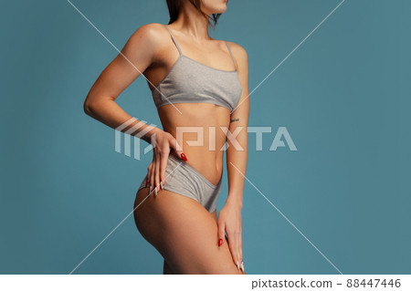 Cropped studio shot of slim, sportive female body in gray cotton underwear posing isolated over blue background. Fitness concept Cropped studio shot of slim, sportive female body in gray cotton underwear posing isolated over blue background. Fitness concept 88447446