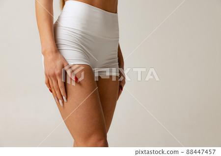 Cropped studio shot of slim, sportive female body in white comfortable underwear isolated over gray background 88447457