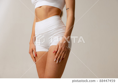 Cropped studio shot of slim, sportive female body in white comfortable underwear isolated over gray background 88447459
