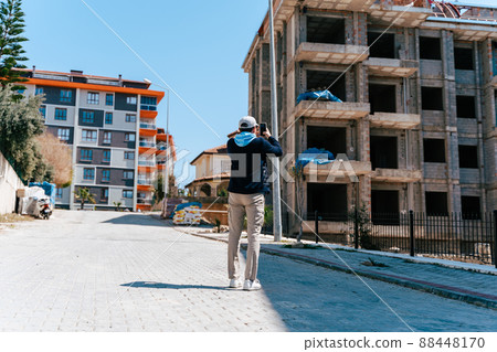 Man taking cellphone photo of development site. Architect engineer estimates building progress. Insurance agent inspects building. Journalist blogger pictures unfinished cancelled house construction Man taking cellphone photo of development site. Architect engineer estimates building progress. Insurance agent inspects building. Journalist blogger pictures unfinished cancelled house construction 88448170