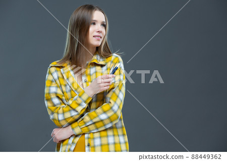 Studio shot of attractive smiling girl looking at camera and holding an electronic cigarette in a raised hand, isolated on grey-blue background 88449362