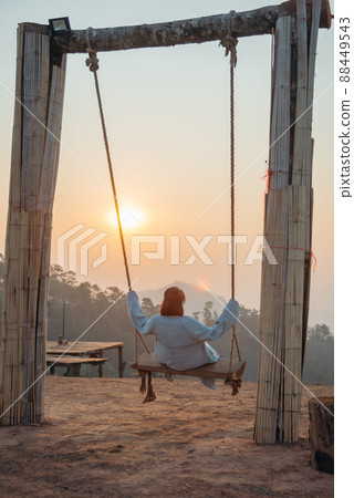 Loneliness woman sitting on the swing and looking at the sun at sunrise time. Loneliness woman sitting on the swing and looking at the sun at sunrise time. 88449543