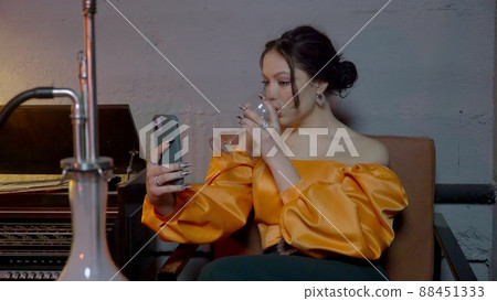 A beautiful young woman drinking alcohol and taking a drag on a hookah takes a selfie on her phone. A girl smokes a hookah in a bar. A beautiful young woman drinking alcohol and taking a drag on a hookah takes a selfie on her phone. A girl smokes a hookah in a bar. 88451333