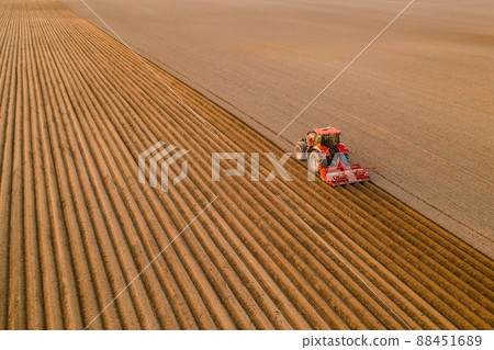 Tractor prepares soil for cultivation dragging plow behind on endless field. Powerful machine works in agriculture at rural site aerial view 88451689