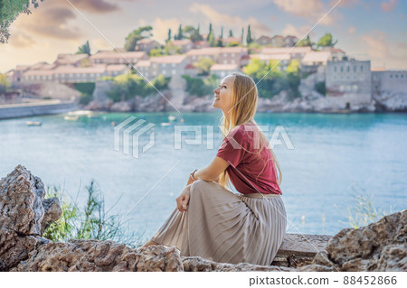 Woman tourist on background of beautiful view of the island of St. Stephen, Sveti Stefan on the Budva Riviera, Budva, Montenegro. Travel to Montenegro concept Woman tourist on background of beautiful view of the island of St. Stephen, Sveti Stefan on the Budva Riviera, Budva, Montenegro. Travel to Montenegro concept 88452866