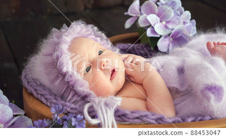 newborn little baby in violet woolen garment lies in wooden basket on dark background 88453047