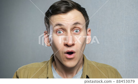 Handsome guy with stylish hairdo surprised to camera over grey background. 88453079