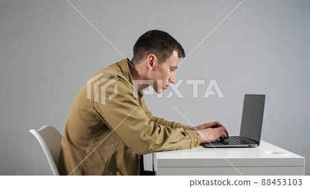 Man employee with crooked neck works on laptop in office Man employee with crooked neck works on laptop in office 88453103