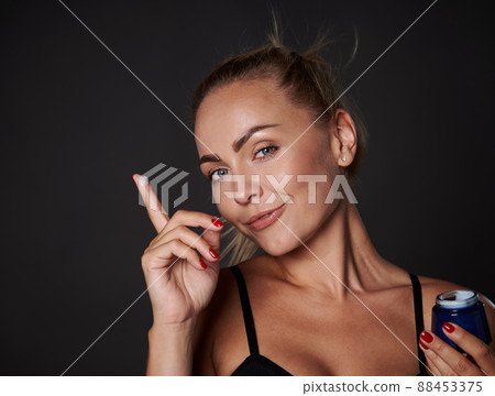 Stunning middle aged blonde pretty woman with healthy glowing tanned skin holding anti wrinkles facial cream, moisturizer. Youth concept and prevention of first signs of aging process. 88453375