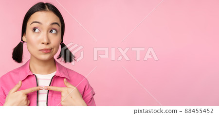 Cute korean girl with silly hairbuns, looking happy and shy, thinkin of smth, posing against pink background 88455452