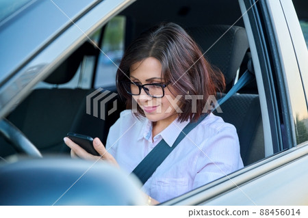 Confident female driver with smartphone driving a car Confident female driver with smartphone driving a car 88456014