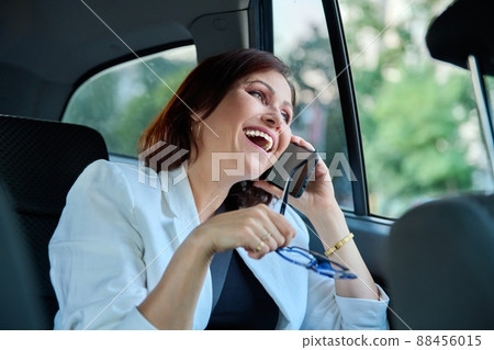 Portrait of middle-aged business woman in car in back passenger seat talking on phone. Portrait of middle-aged business woman in car in back passenger seat talking on phone. 88456015