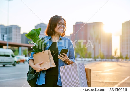 Woman with shopping paper bags, purchased plant walking outdoor 88456016