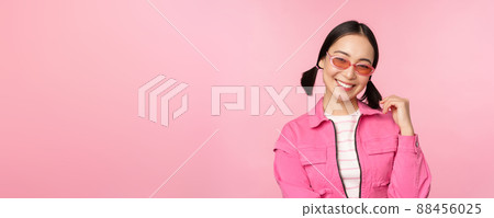 Beautiful asian girl in sunlgasses, smiling at camera, posing against pink studio background Beautiful asian girl in sunlgasses, smiling at camera, posing against pink studio background 88456025
