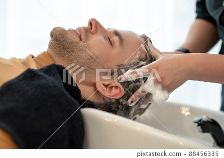 Young man sitting at the chait while having head massage and looking relaxed Young man sitting at the chait while having head massage and looking relaxed 88456335