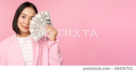 Microcredit, investment and business people concept. Young asian businesswoman, corporate lady showing money, cash dollars, smiling pleased, pink background Microcredit, investment and business people concept. Young asian businesswoman, corporate lady showing money, cash dollars, smiling pleased, pink background 88456702