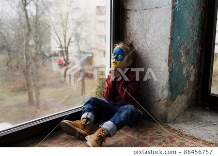 a little Ukrainian patriot girl with the flag of Ukraine on her face prays sitting at the window. Children are against the war in Ukraine 88456757