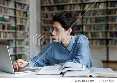 Student guy studying, sits at table with laptop in library 88457199