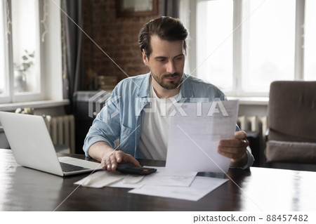 Focused millennial man paying domestic bills, using calculator Focused millennial man paying domestic bills, using calculator 88457482