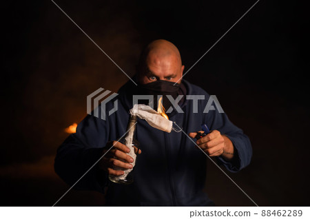A masked man is holding a burning bottle. Molotov cocktail. A masked man is holding a burning bottle. Molotov cocktail. 88462289