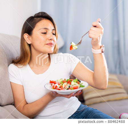 Satisfied housewife sits on a sofa and eats vegetable salad Satisfied housewife sits on a sofa and eats vegetable salad 88462488