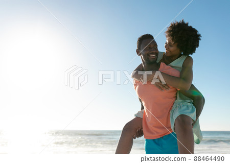 African american man giving piggyback to girlfriend at beach against sky with copy space 88464490