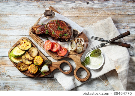 Grilled steak on a cutting board and assorted grilled vegetables. Appetizing grilled meat with vegetables and herbs, sauce. Top view Grilled steak on a cutting board and assorted grilled vegetables. Appetizing grilled meat with vegetables and herbs, sauce. Top view 88464770